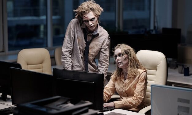 Premium Photo | Young spooky zombie businessman standing next to female colleague sitting by desk in front of computer monitor during teamwork